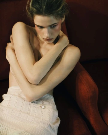 Mila Prvulovic crossing her arms while seated in a red velvet armchair wearing a textured light tweed skirt.