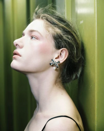 Close-up profile shot of a woman with blonde hair pulled back, wearing a black and silver bow-shaped earring with a dangling pearl.