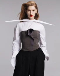 Apolline Rocco Fohrer wearing an exaggerated winged collar shirt, grey corset top, and black trousers against a neutral background.