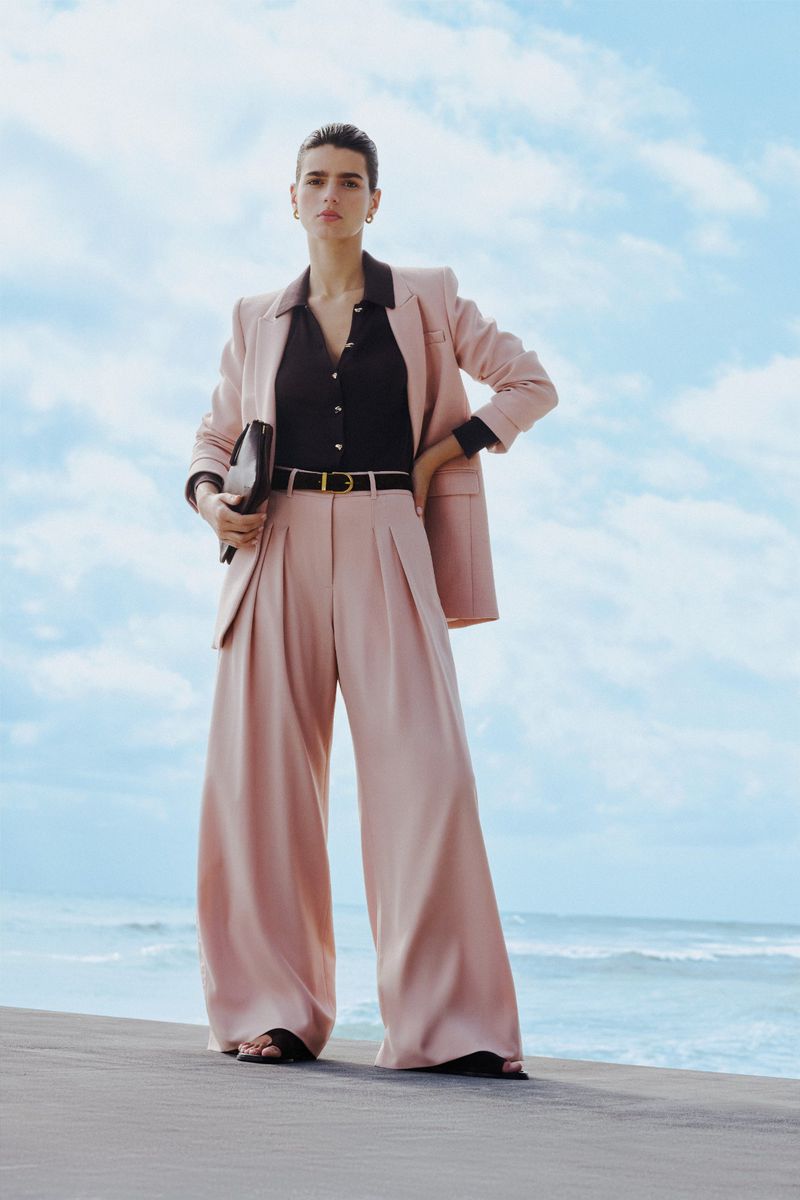 Model Paula Anguera wearing a light pink wide-leg trouser suit and brown shirt by the ocean for ME+EM.