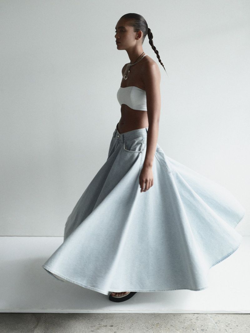 Fashionable woman wearing a white tube top and a large denim skirt with a studio backdrop, captured in a medium shot.