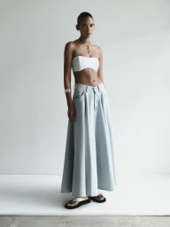 Summer Thompson wearing a white bandeau top and a long light-wash denim maxi skirt against a white studio background.