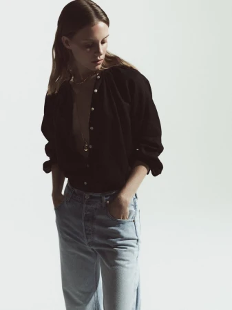 Model Anouk Smits posing in a black button-down shirt and light-wash denim jeans against a white backdrop.