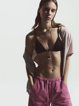Model wearing pink trousers, black bralette, and striped shirt against white studio seamless background