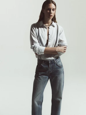 Model Anouk Smits wearing an unbuttoned white shirt and blue denim jeans with crossed arms against a neutral studio backdrop.