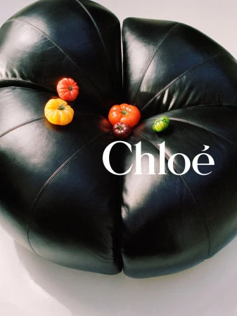 Close-up of a black leather pouf adorned with an arrangement of colourful tomatoes, presented against a soft white backdrop.