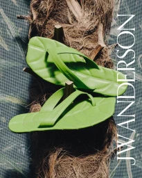Bright green quilted leather flip flops mounted on fibrous palm trunk bark with JW Anderson lettering on the right.