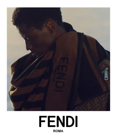 Male model poses with a brown Fendi towel draped over his shoulder, bag with a signature pattern, and the Fendi logo in the foreground.