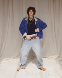 Mathilda Gvarliani poses in an oversized blue jacket and wide trousers against a draped cream fabric backdrop.