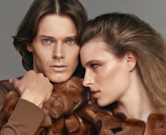 Portrait of a man and a woman with brown hair, the man with his arms wrapped around the woman, both wearing earth-tone clothing.