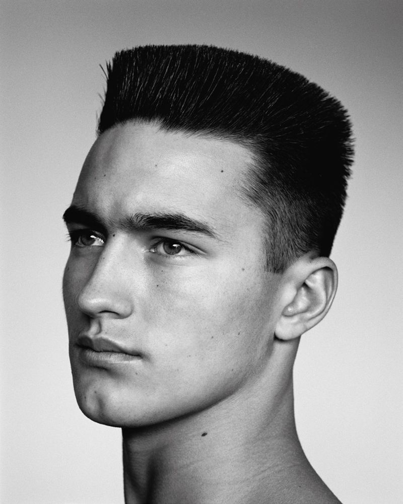 Black and white portrait of a young adult male with a flattop haircut, gazing off-camera against a neutral background in a photo studio.