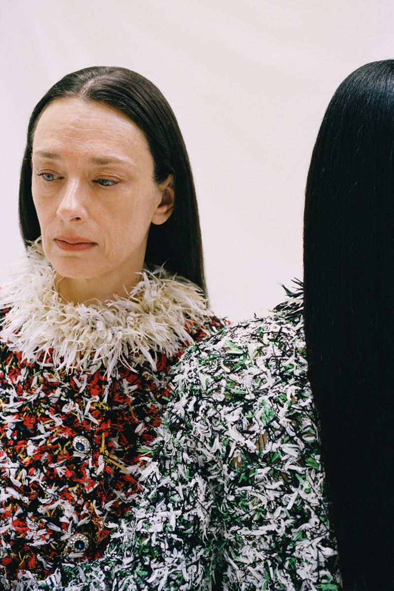 Two adult women pose in a photo studio wearing intricately decorated coats with feathered collars against a plain white background.