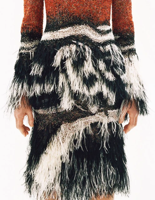 Close-up of a fashion dress with a blend of warm orange hues fading into black, contrasted by white horizontal bands and feather-like accents.