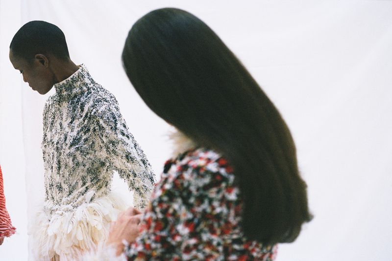 Two women in patterned tops pose in front of a white backdrop, one with long black hair and the other in a textured white top.