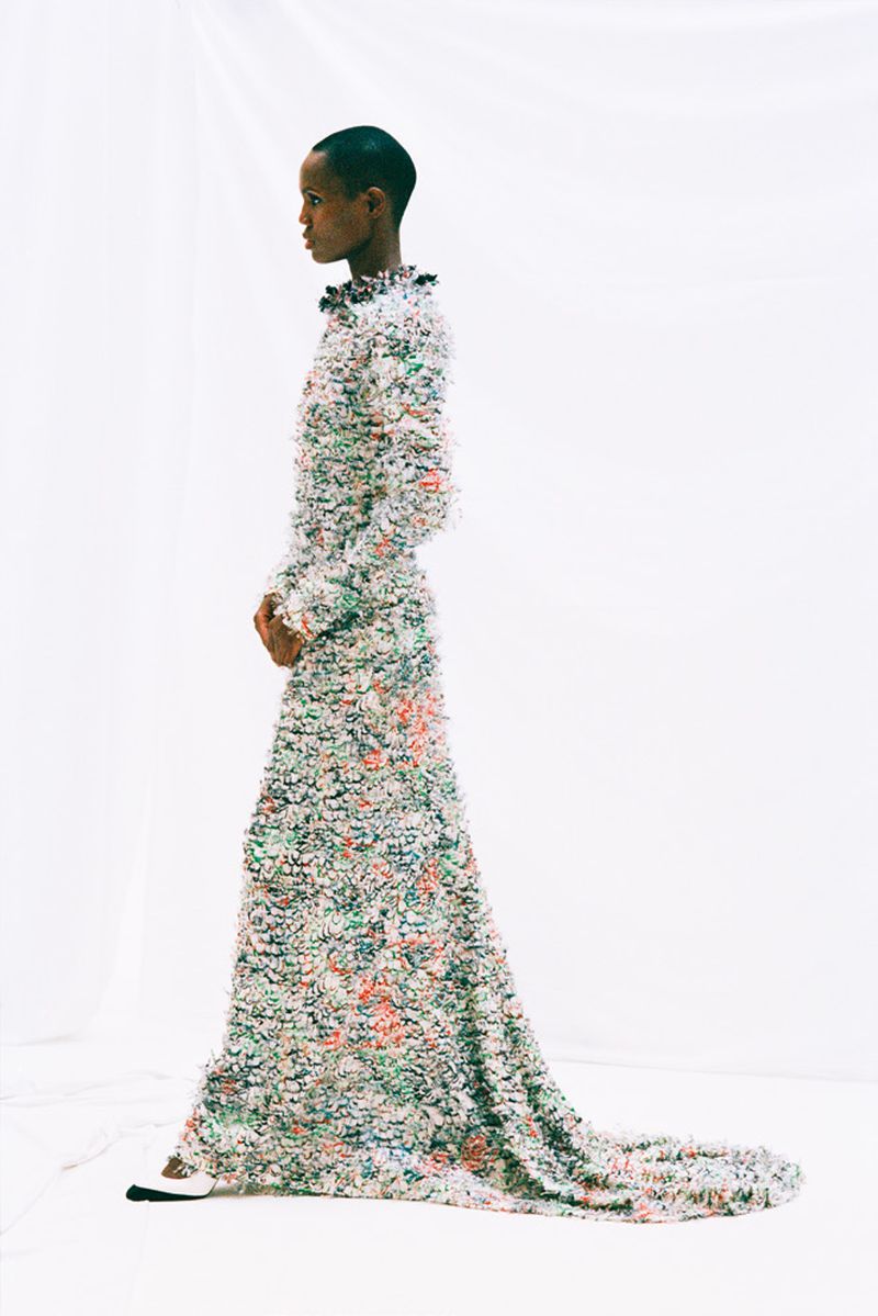 Adult female fashion model posing in long, floral, couture gown with train. Side view in brightly lit photo studio with white backdrop.