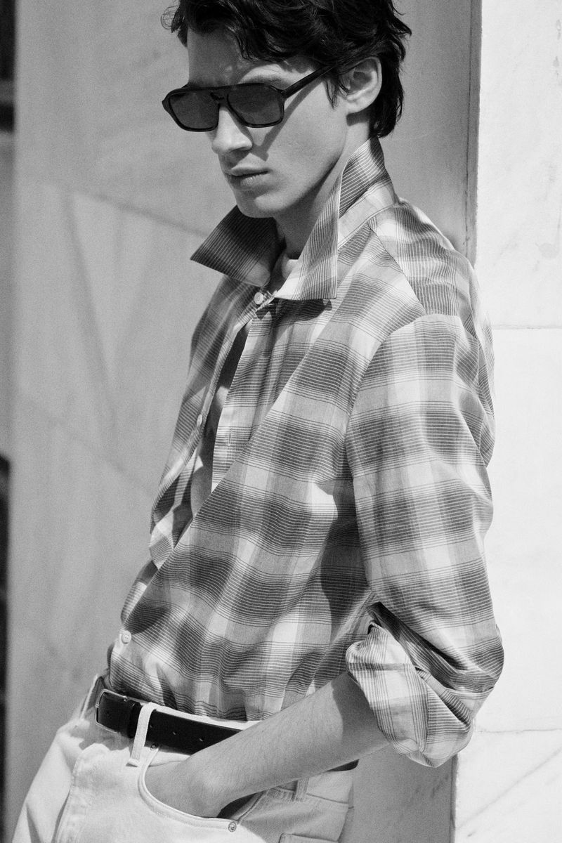 Monochrome portrait of a young male model wearing sunglasses and a patterned button-down shirt outdoors.