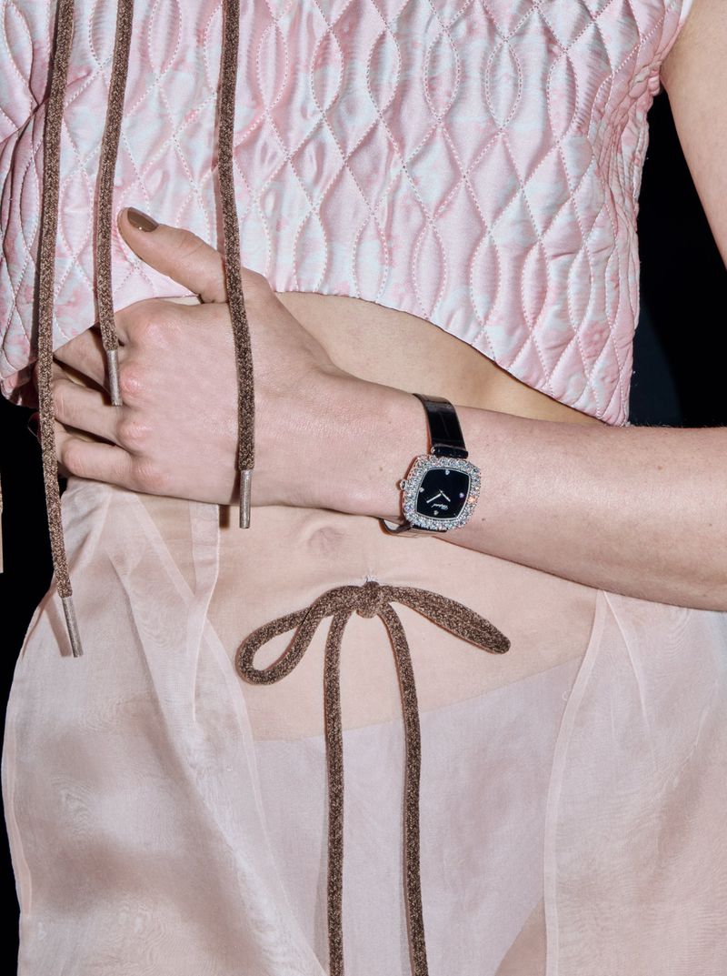 Close-up shot of a light-skinned person wearing a pink quilted top and a watch, featuring brown laces tied around their midriff.
