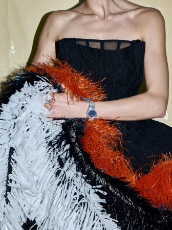Close-up of a person wearing a strapless black dress with orange, black, and white fringe, adorned with a sparkling silver wristwatch.