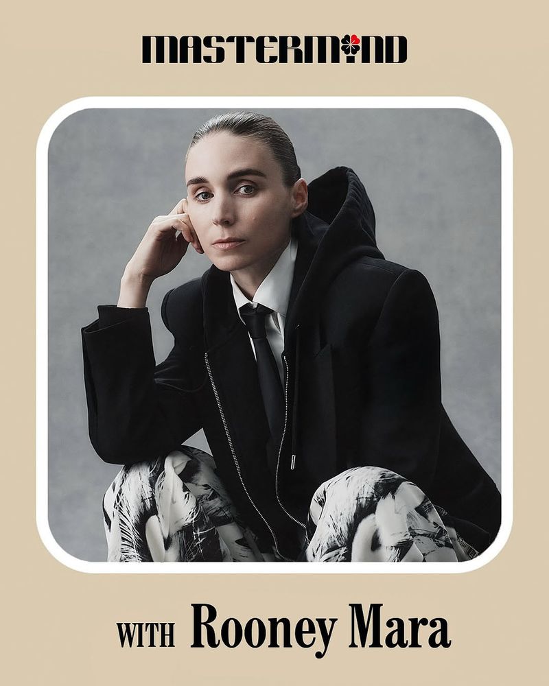 Rooney Mara portrait in hooded blazer, tie, and graphic pants against gray backdrop; Mastermind branding above, presented in a beige frame.