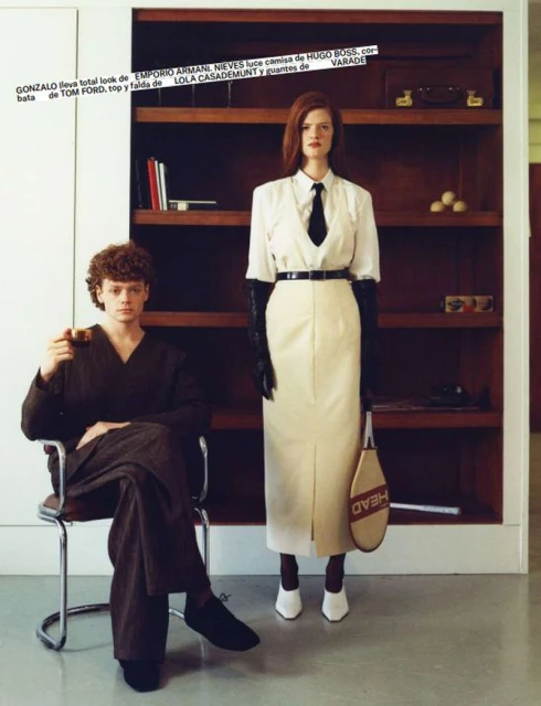 Editorial fashion shot of a man seated with a drink and a woman standing with a tennis racket in an indoor setting.