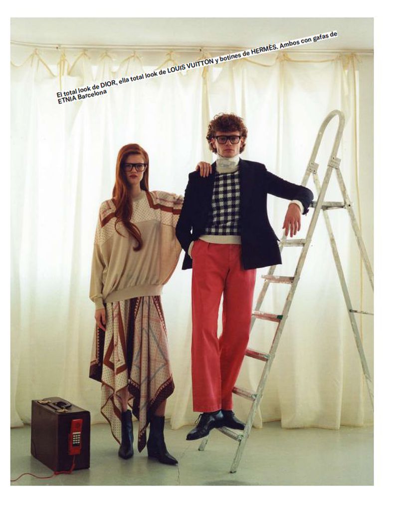 Fashion models Nieves Boucher in a beige patterned outfit and a male model in red trousers posing by a ladder against white curtains.