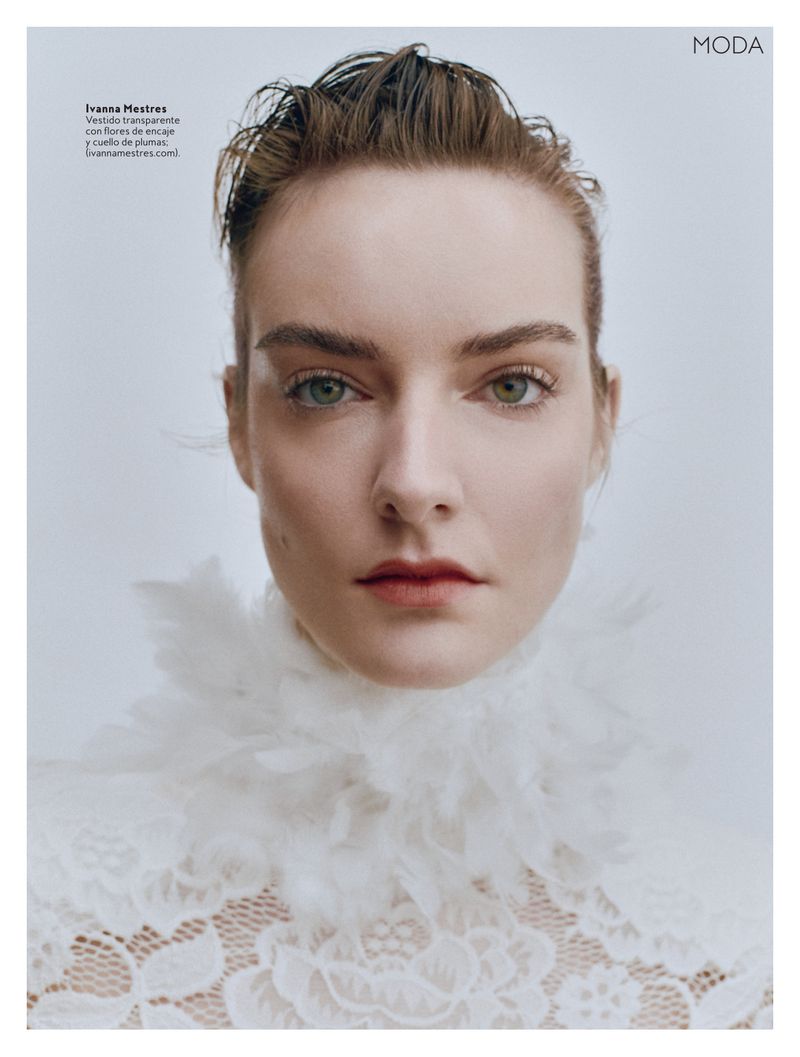 Close-up fashion portrait of a fair-skinned young adult female with light eyes, wearing lace and feathers against a light background.