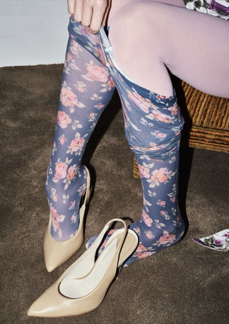 Woman with floral patterned tights and beige heels on a brown carpet, partially undressed in an indoor environment. Fashion studio shot.