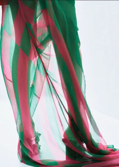 Sheer green and pink patterned fabric draping over legs in high heels against a plain white studio background.