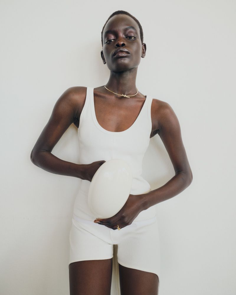 Woman with dark skin and short hair in a white tank top and shorts poses with a white ball against a white backdrop.