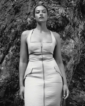 Monochrome portrait of a woman in a fitted top and skirt posing in front of a textured tree trunk in an outdoor setting.
