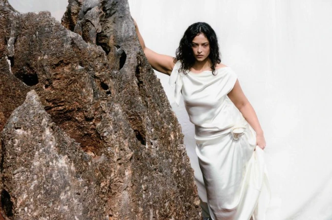 Woman in a white gown poses next to a large rock formation against a white background, portrait framing, studio lighting. 