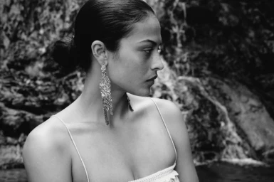 Black and white portrait of a woman wearing textured drop earrings against a rocky natural background