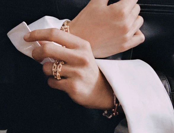 Close-up of model Vivienne Rohner wearing gold chain link rings and a bracelet with oversized white French cuffs.