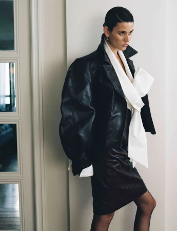 Vivienne Rohner wearing an oversized black leather jacket and white bow blouse beside a glass door.