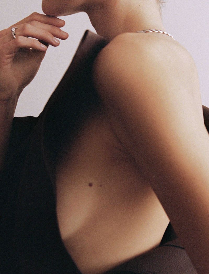 Model Vivienne Rohner posing in a dark backless structured top with a silver chain necklace against a light backdrop.
