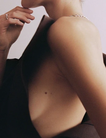 Model Vivienne Rohner posing in a dark backless structured top with a silver chain necklace against a light backdrop.