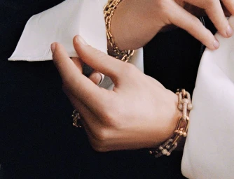 Close-up of model Vivienne Rohner wearing chunky gold link chain bracelets with diamond accents alongside crisp white shirt cuffs.