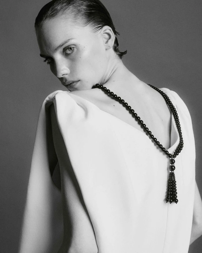 Model Penelope Ternes looking over her shoulder in a white backless top and black beaded tassel necklace.