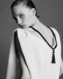 Model Penelope Ternes looking over her shoulder in a white backless top and black beaded tassel necklace.