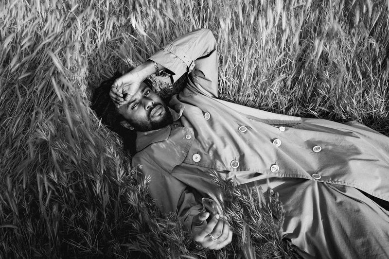 Adult male in a jacket lies in a grassy field in a black and white photograph taken at eye-level in an outdoor environment.