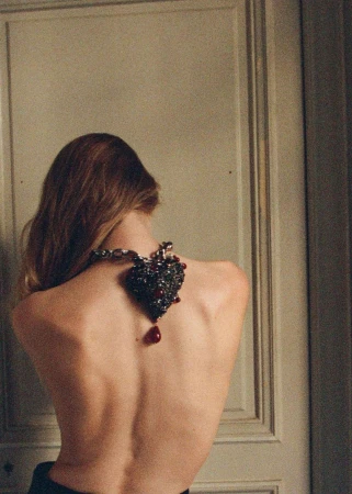 Fashion portrait of a woman's back and shoulders, featuring a large, ornate heart-shaped pendant necklace with a red drop.