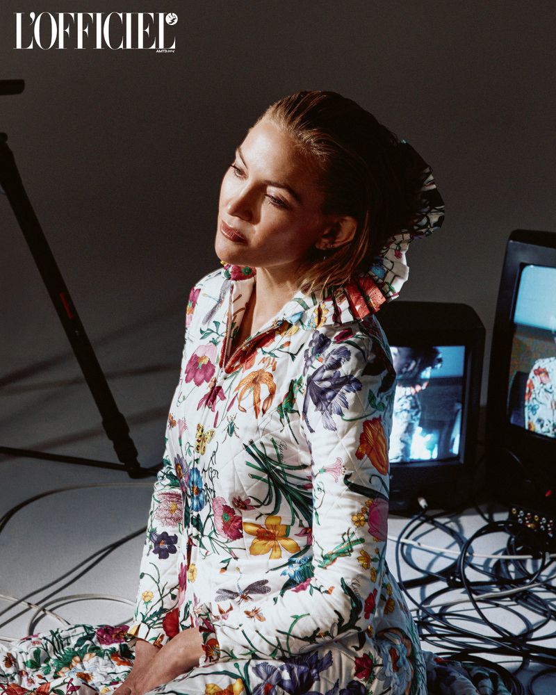 Woman in floral jacket poses in photo studio with vintage TV monitors and cables, editorial fashion for L'Officiel magazine.