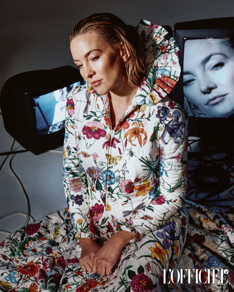 Glamorous portrait of a seated woman in a floral jacket, featuring vintage television set and soft studio lighting.