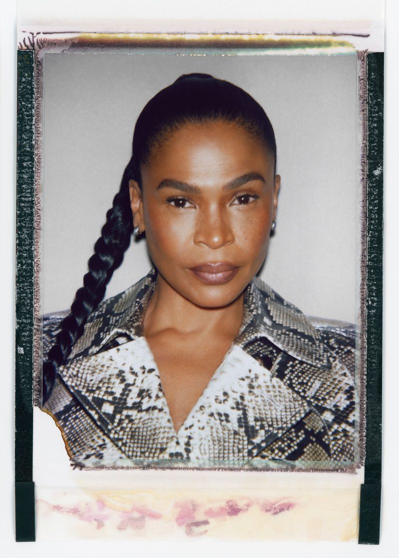 Close-up Polaroid portrait of an adult woman with braided hair and snake-print jacket, set against a plain off-white background.