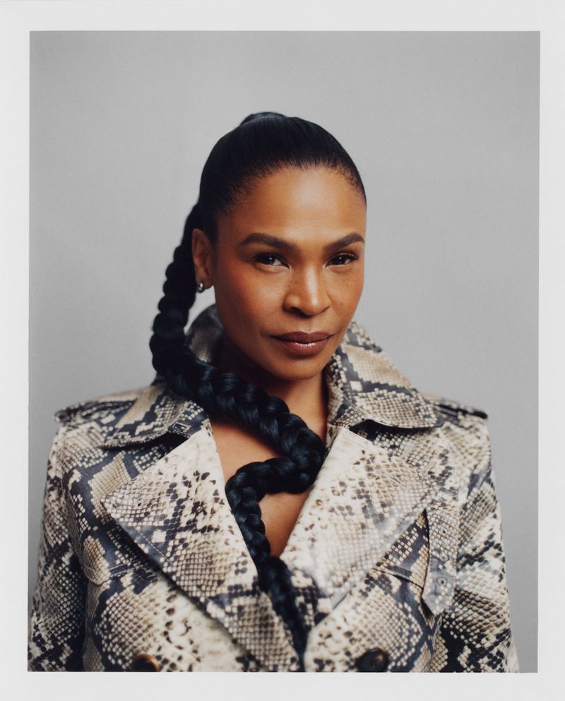 Elegant portrait of a woman with a long, braided ponytail wearing a snakeskin print coat against a neutral grey backdrop in a photo studio.