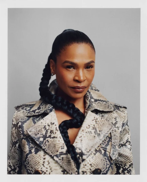 Elegant portrait of a woman with a long, braided ponytail wearing a snakeskin print coat against a neutral grey backdrop in a photo studio.