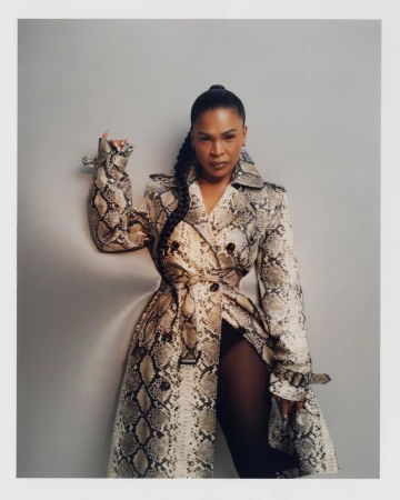 Studio shot of an adult woman in a snakeskin-pattern trench coat with a ponytail, against a neutral background, fashion editorial.