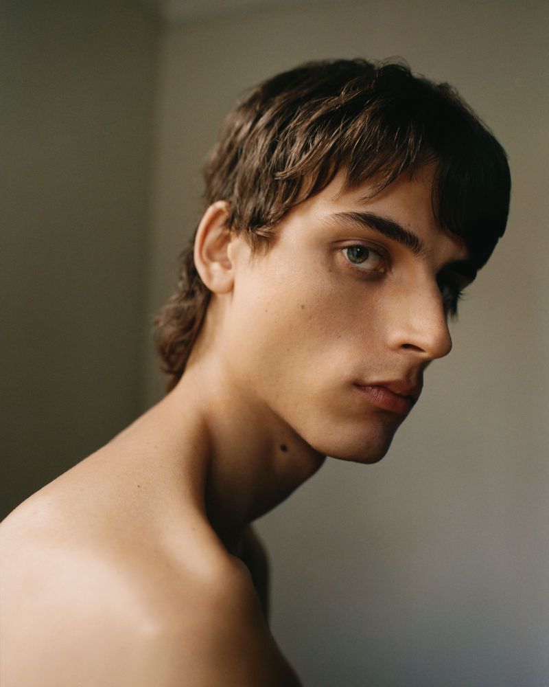 Close-up studio portrait of a young adult male with brown hair and bare shoulders, looking to the side with a serious expression.
