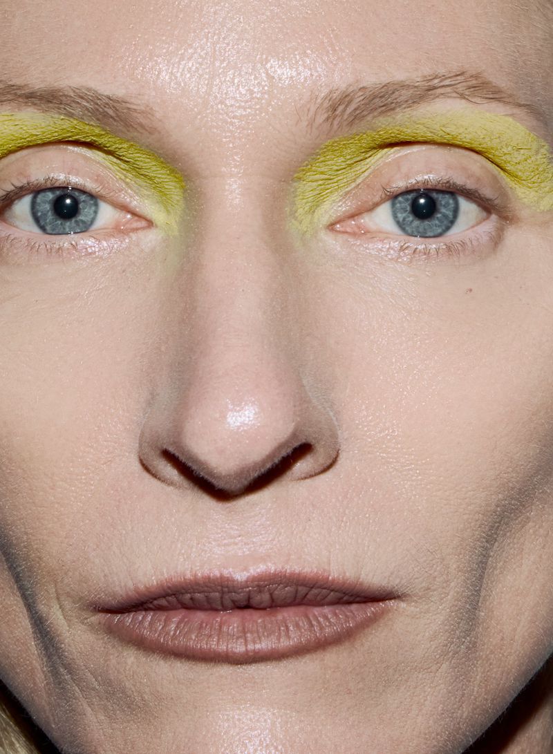 Extreme close-up studio portrait of an adult woman with blue eyes and yellow makeup on her eyebrows. Beauty shot for fashion and cosmetics.