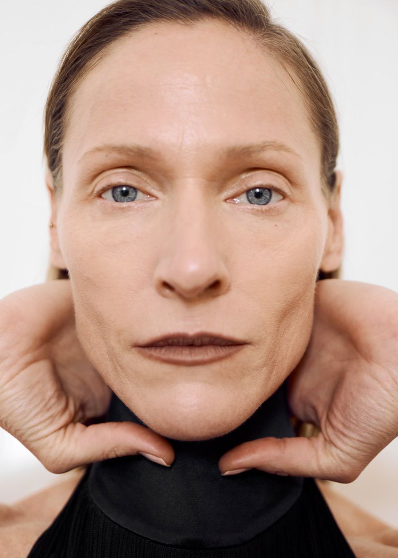 Close-up portrait of model Lindsay Sullivan framing her jawline with her hands against a plain white background.